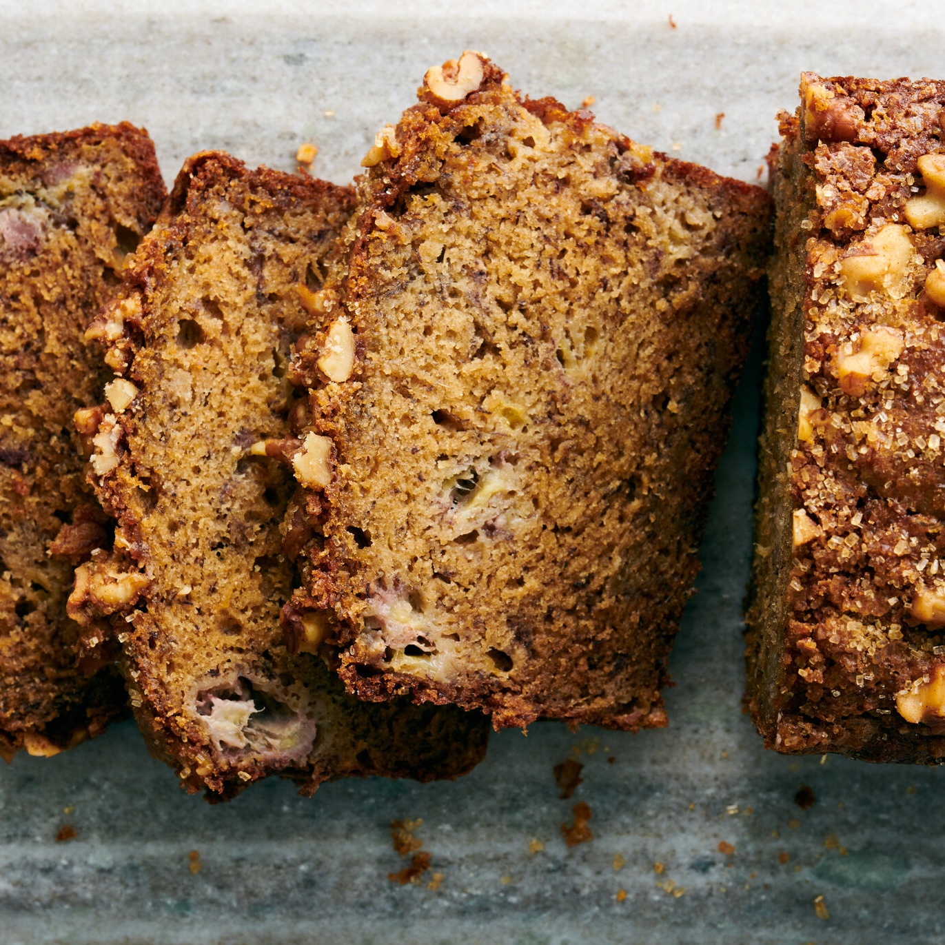 Slices of banana bread with browned crust and nut topping arranged on a stone serving surface