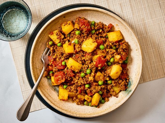 A bowl of spiced minced beef with tomatoes, peas, and golden potato chunks.