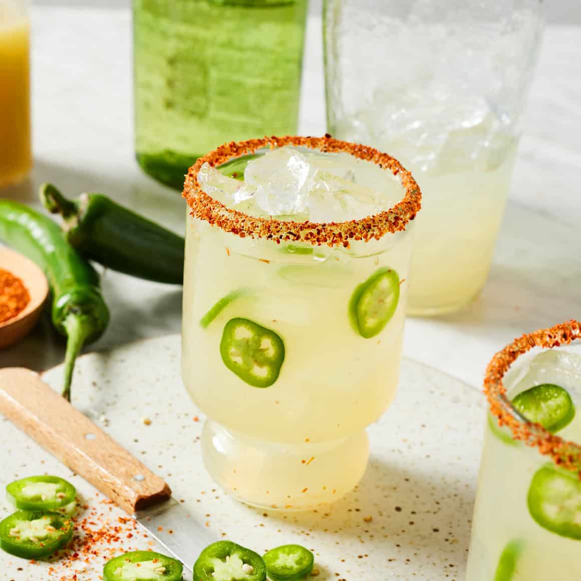 Pale jalapeño margarita in a Tajín-rimmed glass with ice and fresh jalapeño slices.